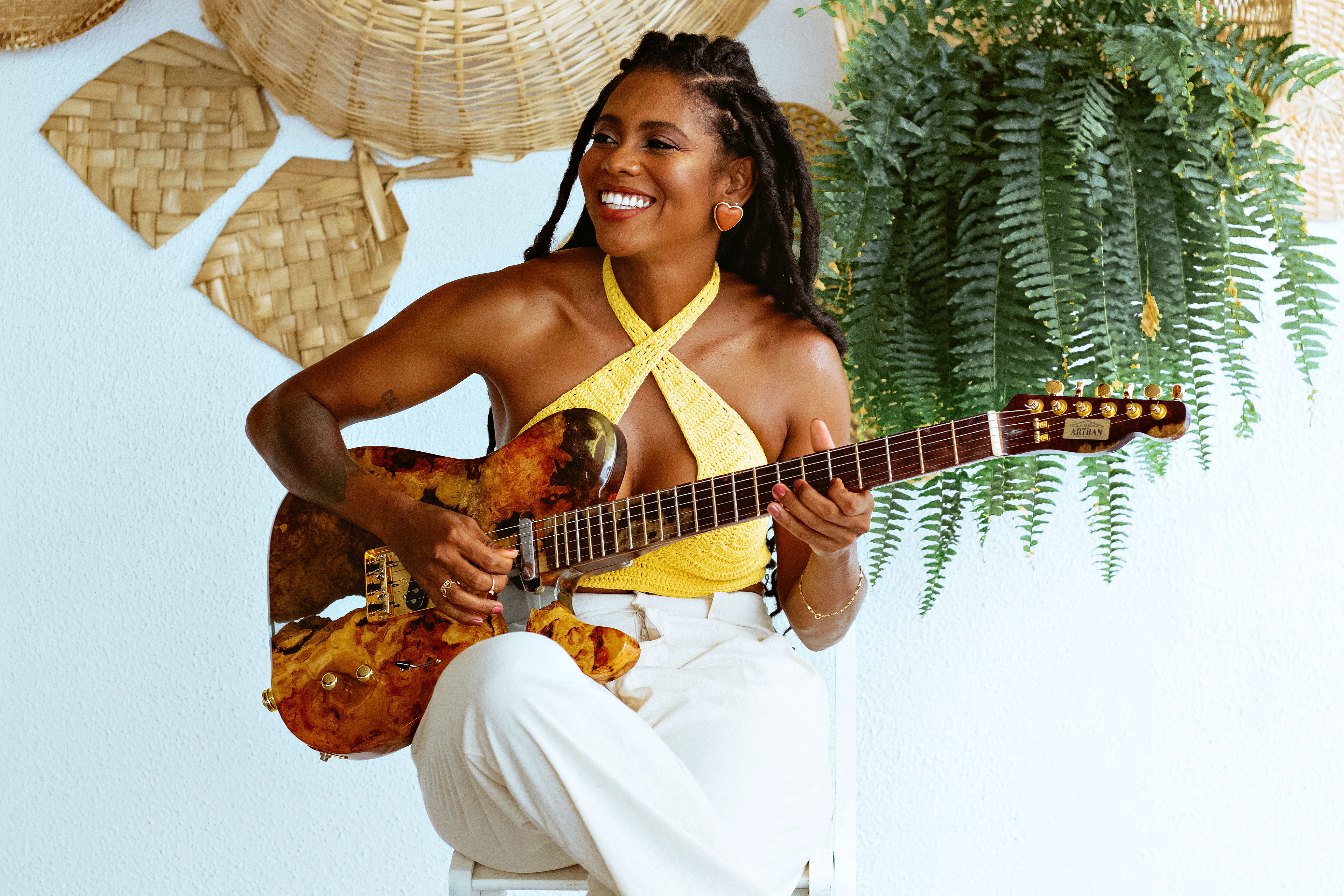 Smiling woman with braided hair playing guitar in a boho setting, Salvador, Brazil.