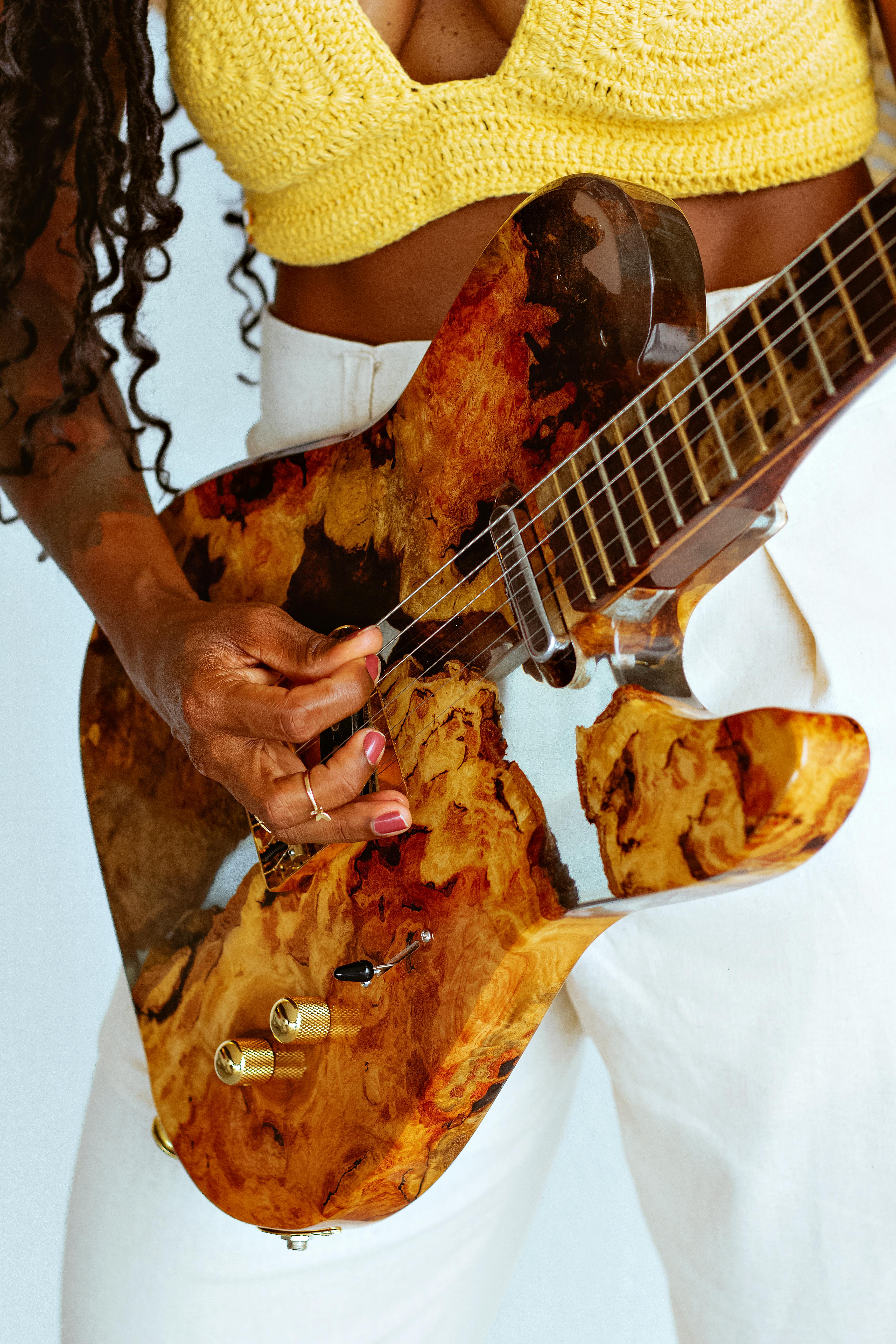 African American woman strumming a custom-designed guitar in a fashion-forward setting.