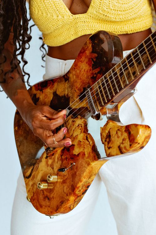 Free African American woman strumming a custom-designed guitar in a fashion-forward setting. Stock Photo