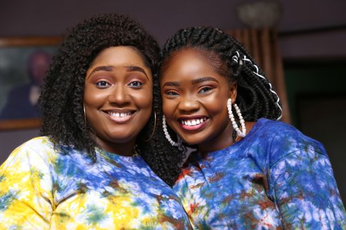 Free A joyful portrait of a mother and daughter wearing colorful tie-dye shirts, smiling indoors. Stock Photo