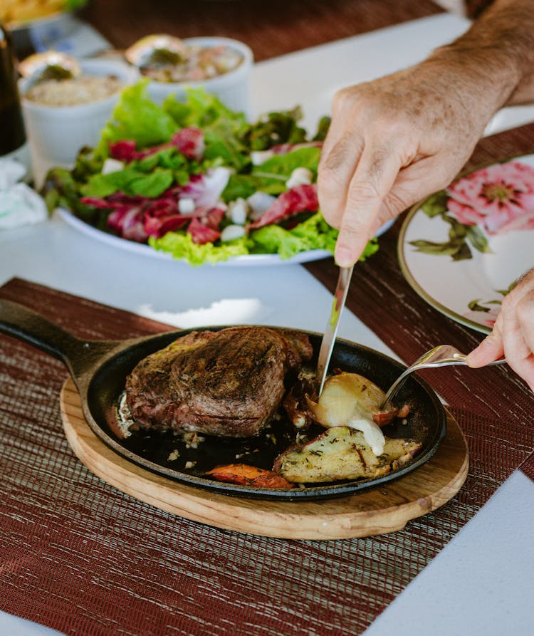 Close-up Of A Person Using A Fork And Knife To Eat A Meat Dish 