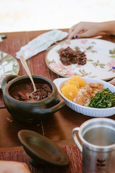 Close-up of a traditional Brazilian feijoada meal with vibrant sides on a rustic table.