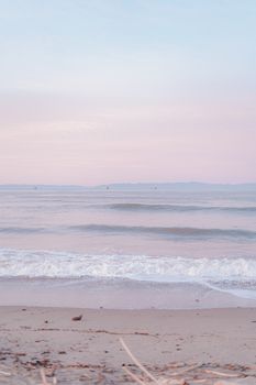 Calm waves gently kissing the tranquil sandy beach under a pastel sky at dawn.