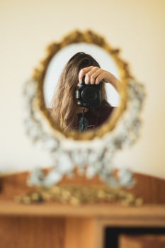 A woman takes a selfie with a DSLR camera in an ornate oval mirror indoors.