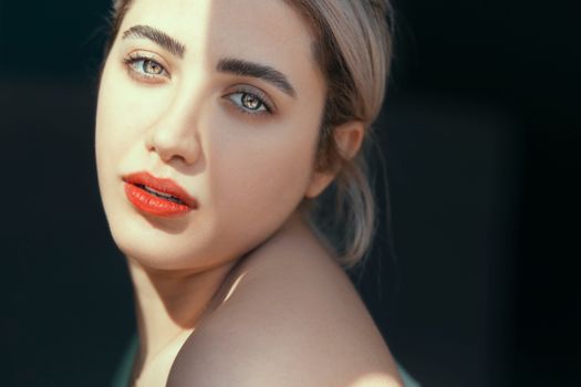 Close-up portrait of a young woman with blonde hair and red lips, softly lit.