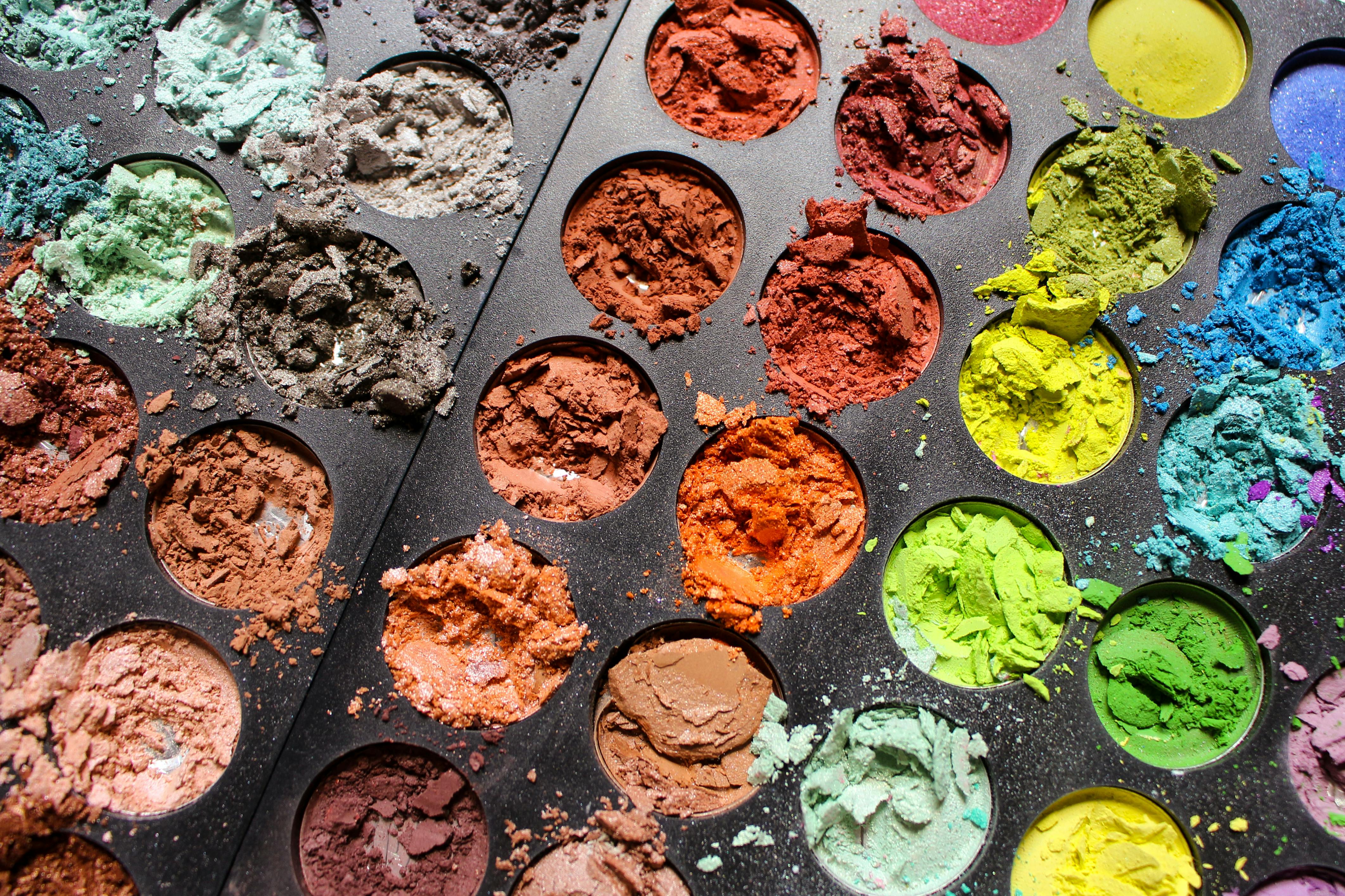 Close-up of a colorful eyeshadow palette with various shades and textures in a tray.