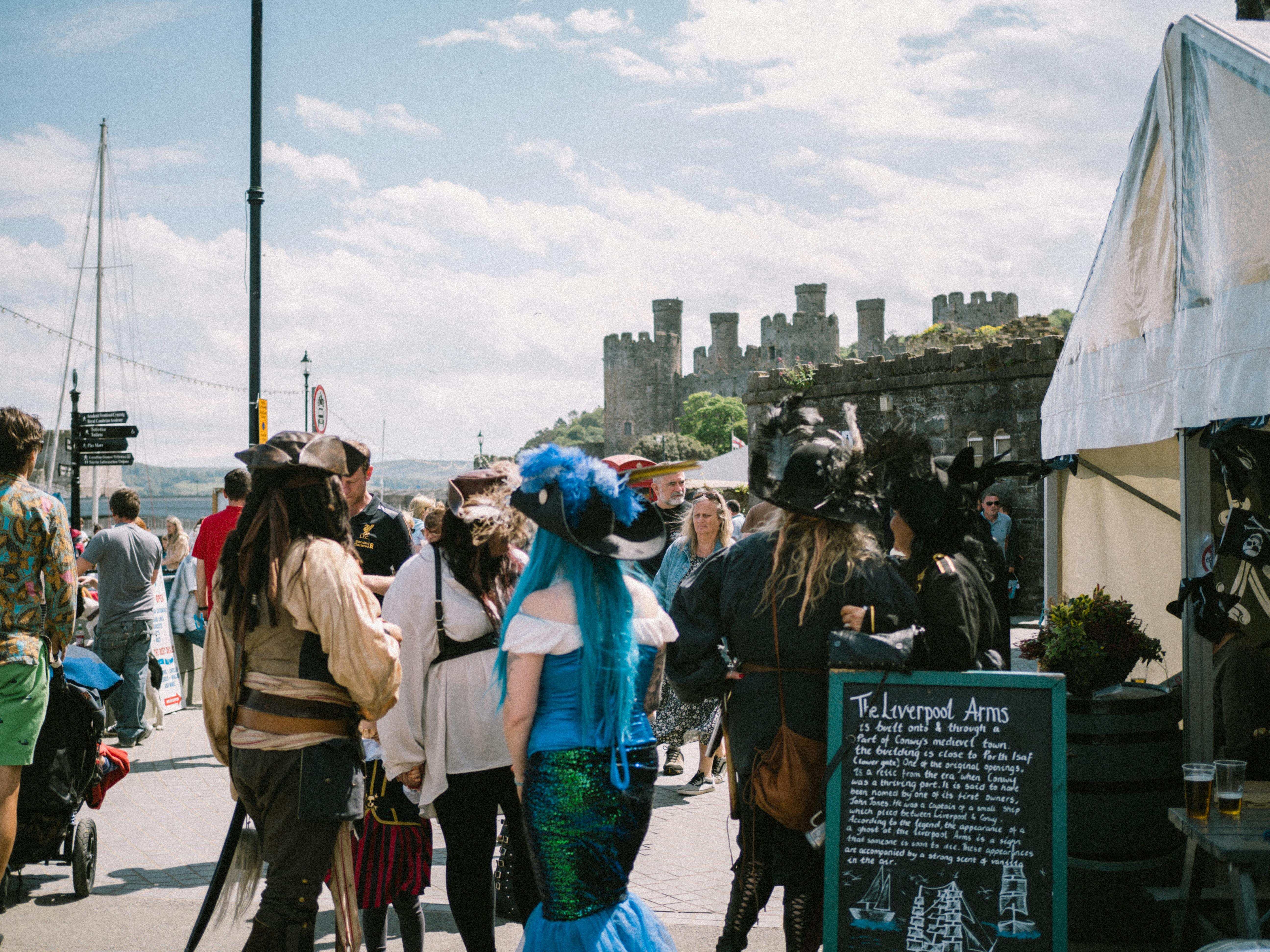 A lively medieval-themed event with attendees in costume by a historic castle.