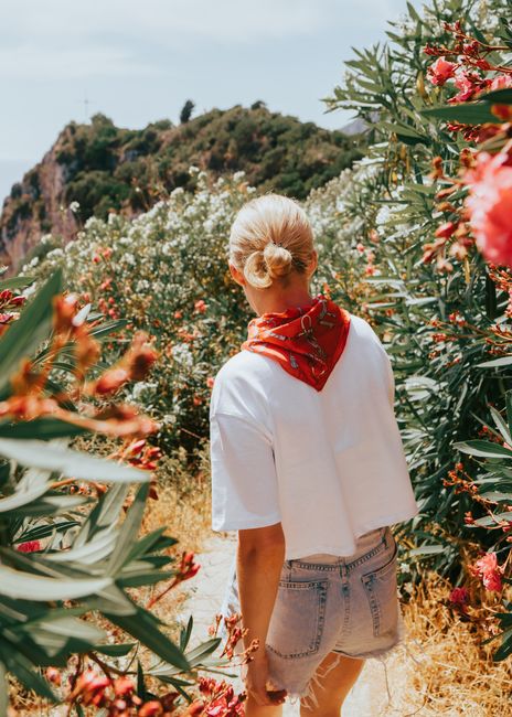 A woman walks through vibrant flowers in Kerkyra, Greece on a sunny day.
