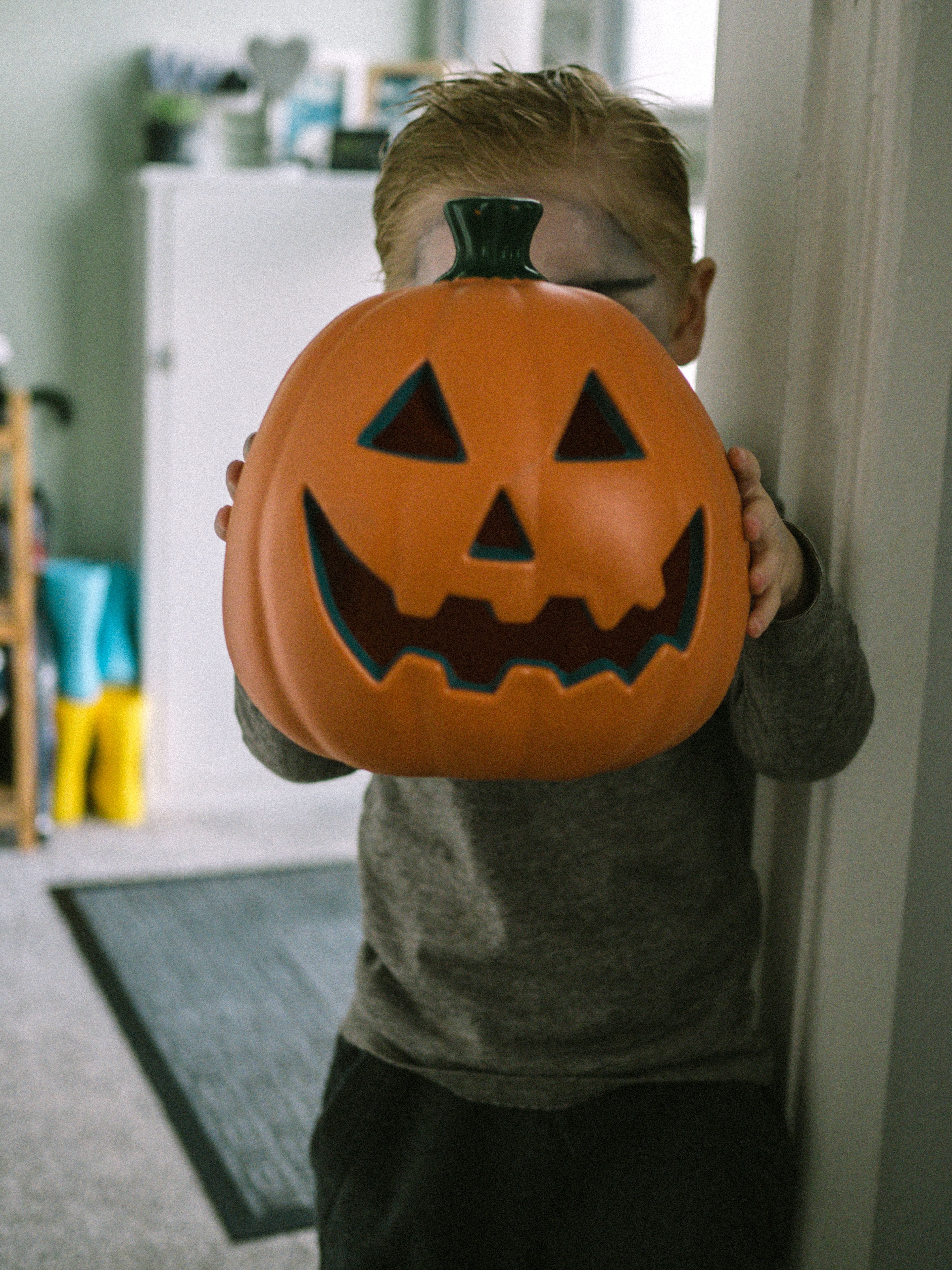 Young child holds a smiling jack-o'-lantern indoors, celebrating Halloween.