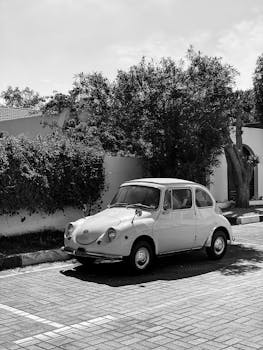 Monochrome shot of a classic vintage car parked outdoors against a green hedge, evoking nostalgia.