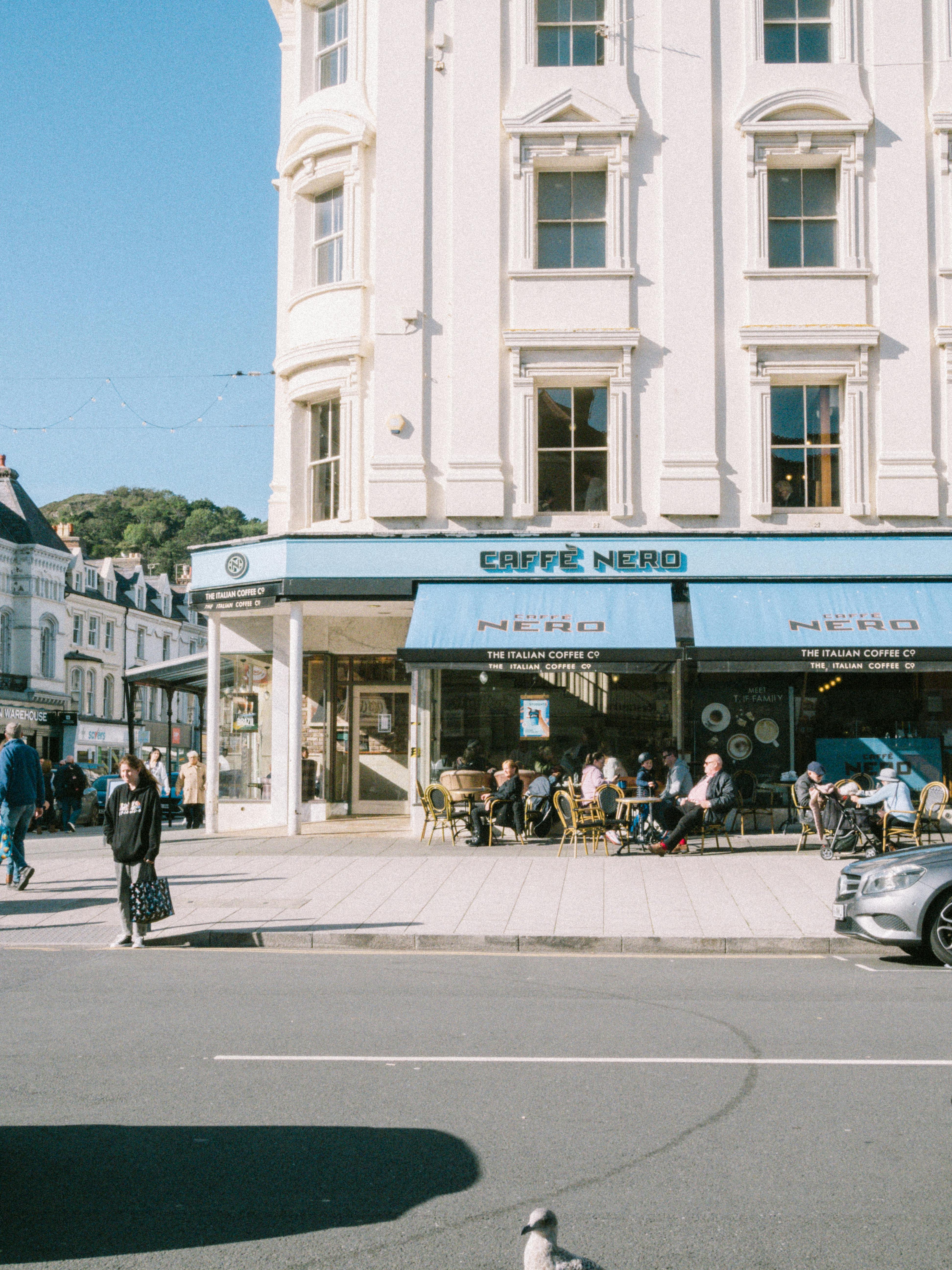 Captivating street view in Llandudno, Wales, featuring a sunlit café and lively sidewalk scene.