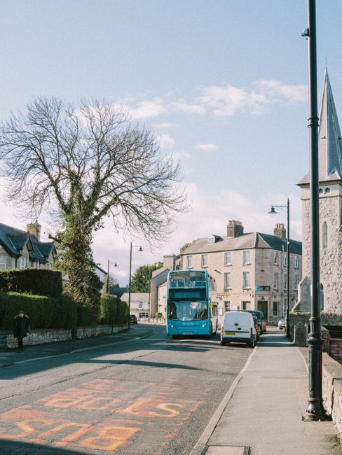 Peaceful town street scene with a blue bus passing by old stone buildings on a sunny day.