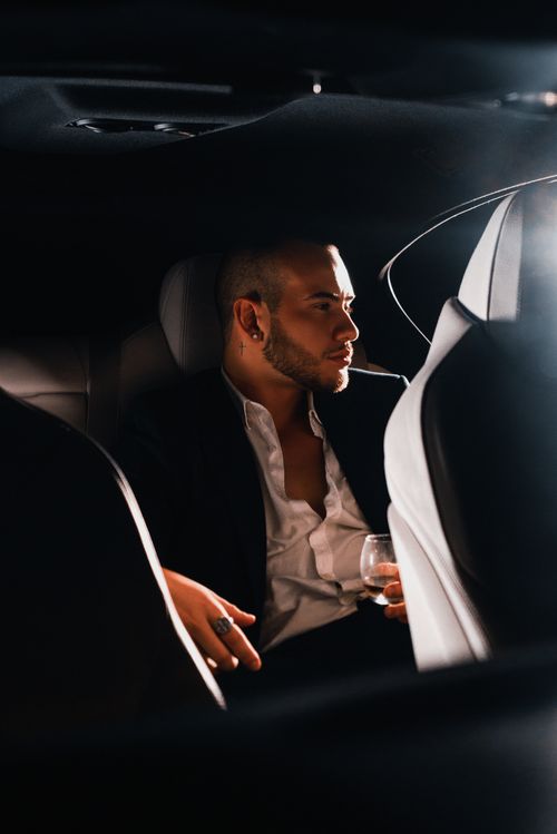 Free Elegant man with a drink sitting in a car interior, exuding sophistication in a refined setting. Stock Photo
