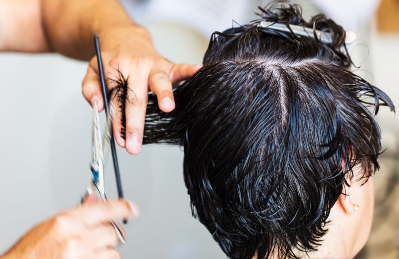 Close-up of a stylist cutting dark, wet hair in a salon setting, showcasing the precision and technique of hairstyling.