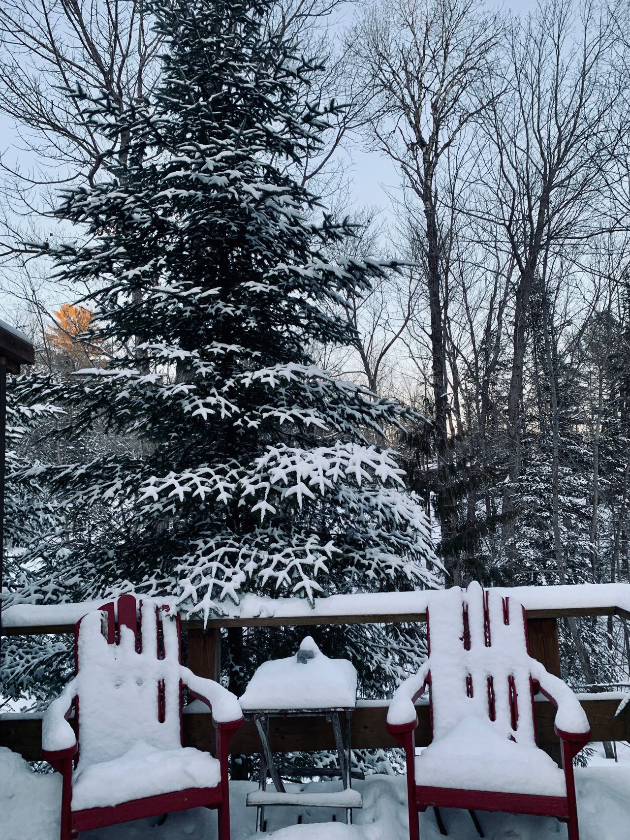 Two red Adirondack chairs and a small table buried in deep snow on a cabin deck in Huntsville, Ontario.