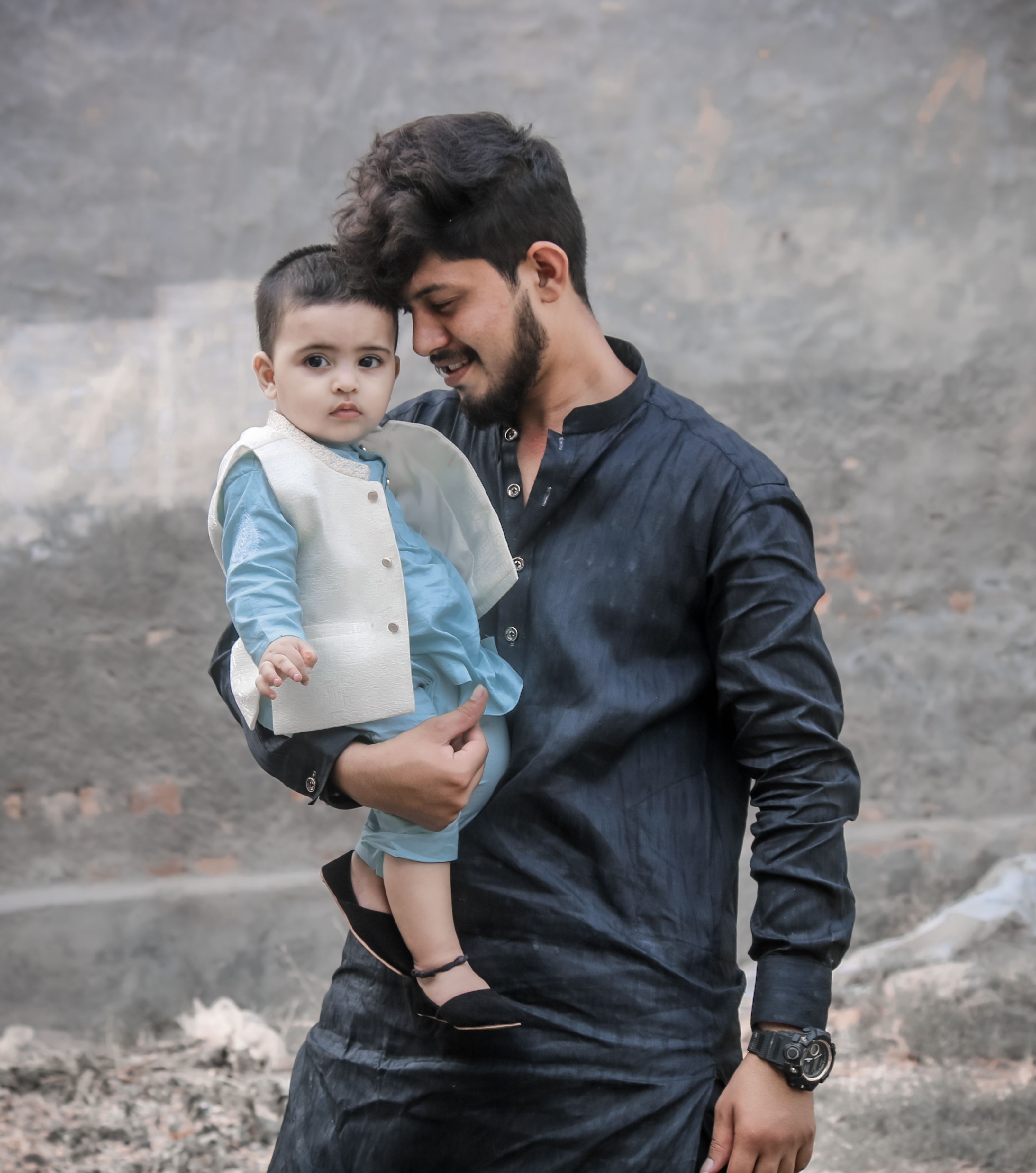 A heartwarming moment of a father holding his son in traditional Pakistani clothing outdoors.