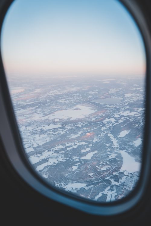 Free Scenic winter aerial view through airplane window over snowy terrain. Stock Photo