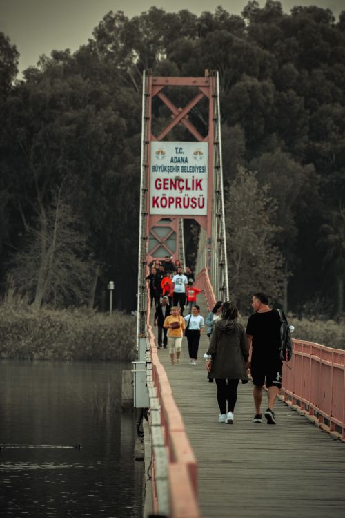 Free Tourists and locals walking on the Gençlik Bridge in Adana, Turkey, amidst a scenic outdoor setting. Stock Photo