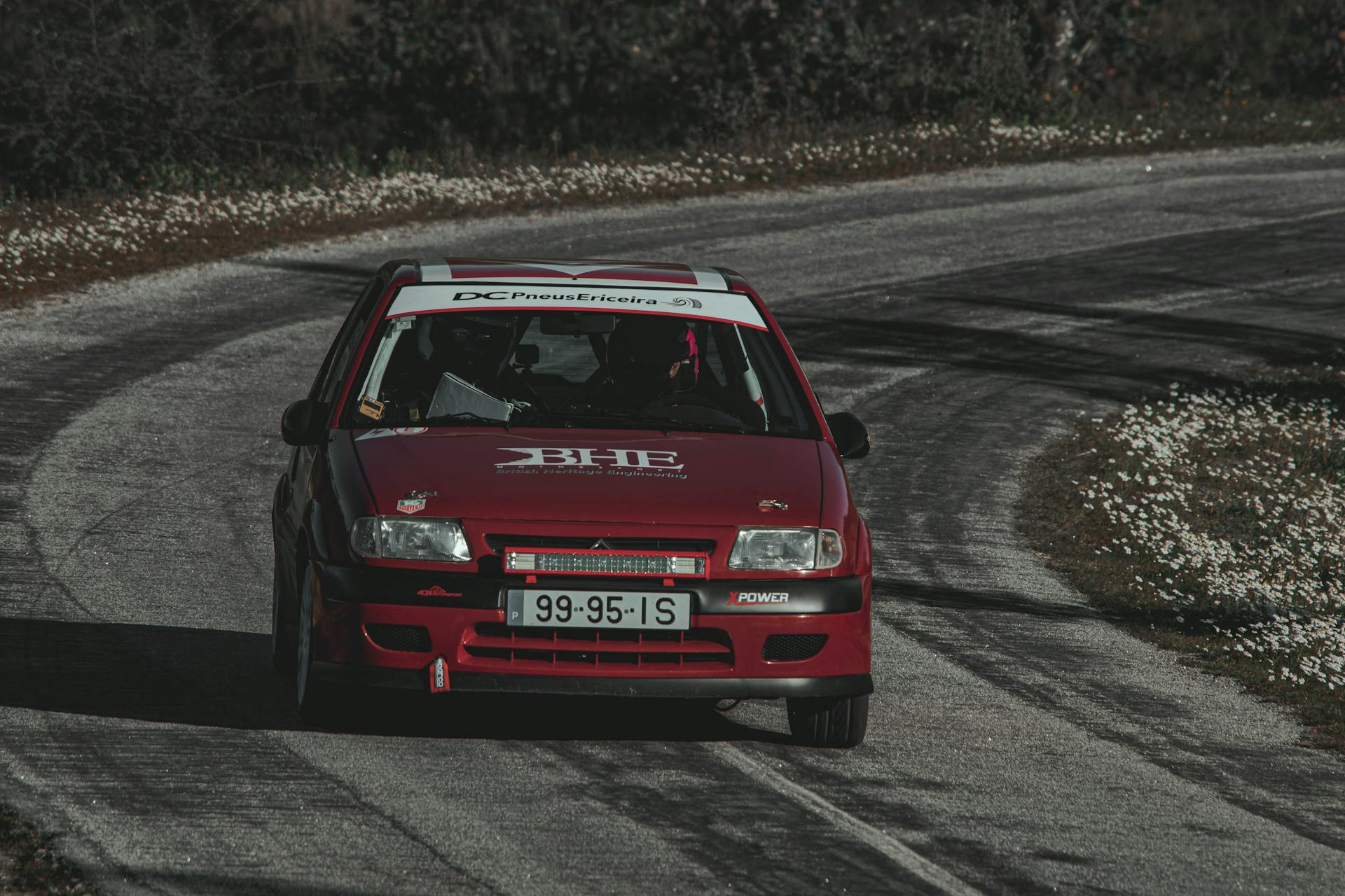 Red Citroen Saxo race car driving on winding asphalt track, showcasing speed and motorsport action.