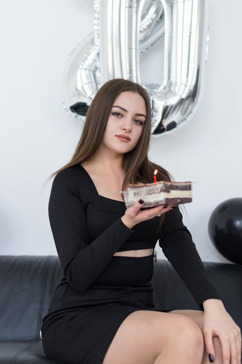 Young Brunette Sitting on a Sofa with a Small Birthday Cake 