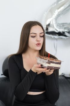A young woman blows out a candle on a birthday cake surrounded by balloons, adding to the celebration mood.