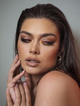 Close-up portrait of a woman with golden makeup and white nail polish, exuding elegance and glamour.