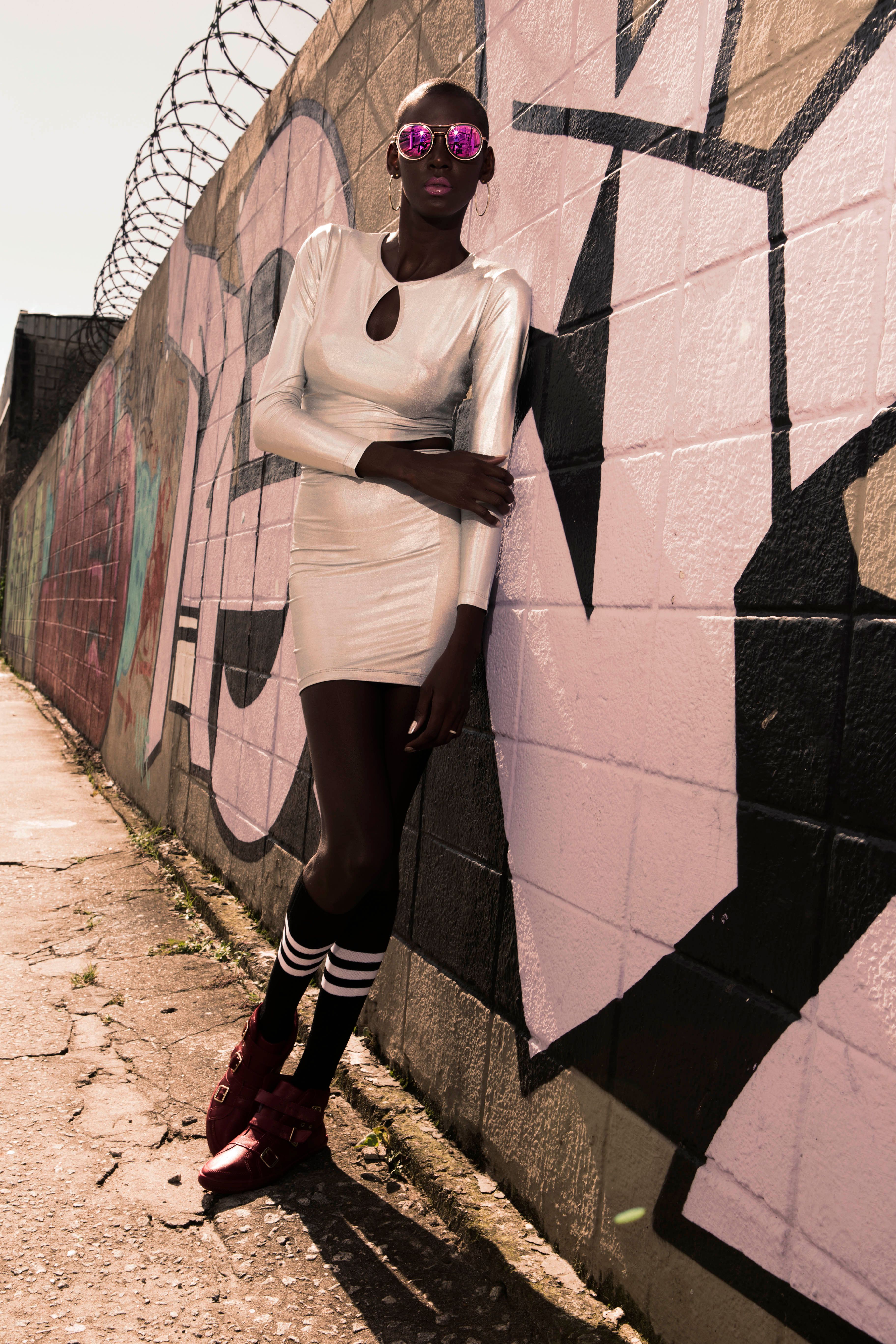 Fashionable woman in chic white dress leaning against vibrant graffiti wall.