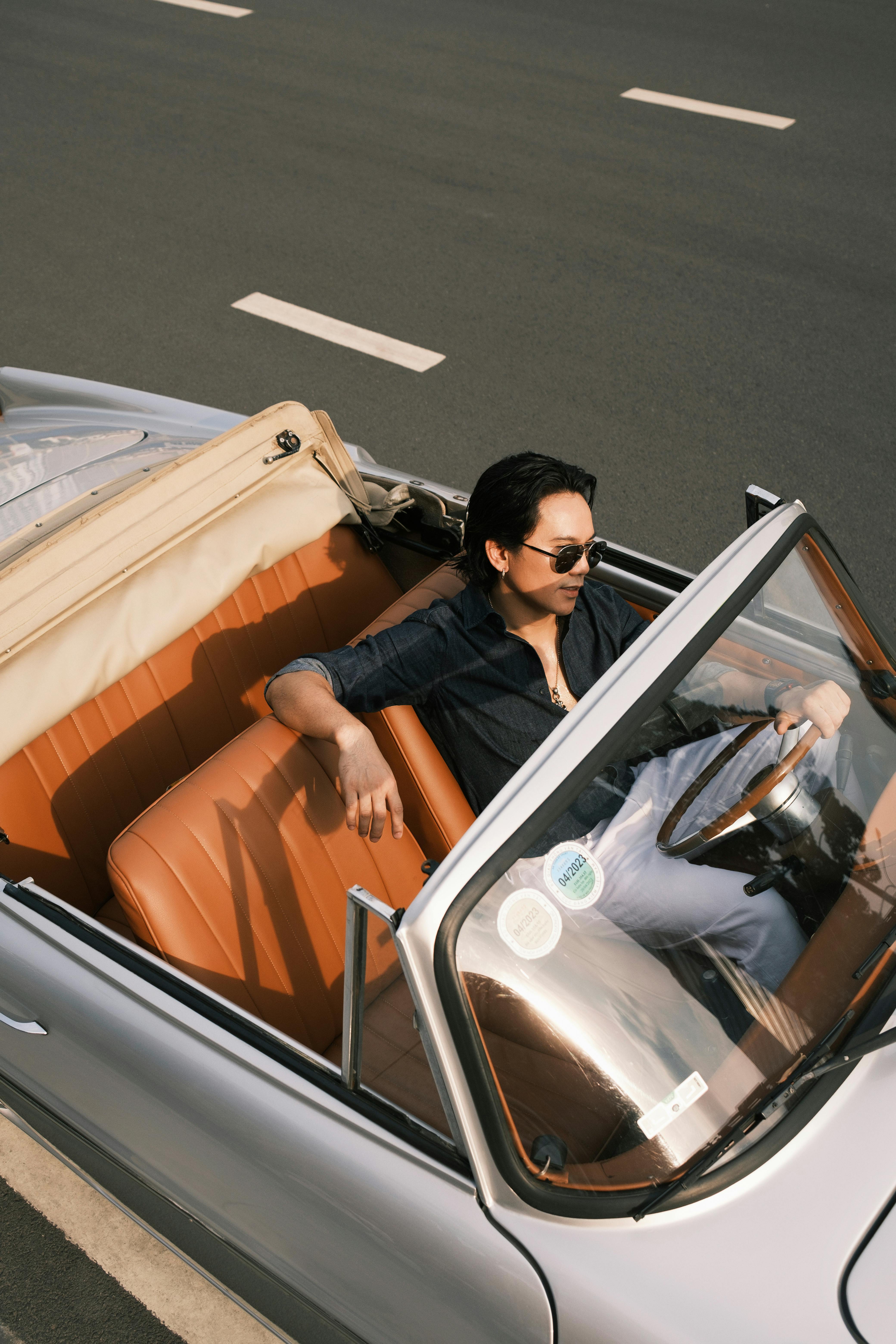 A man enjoying a drive in a vintage convertible car on a sunny day.