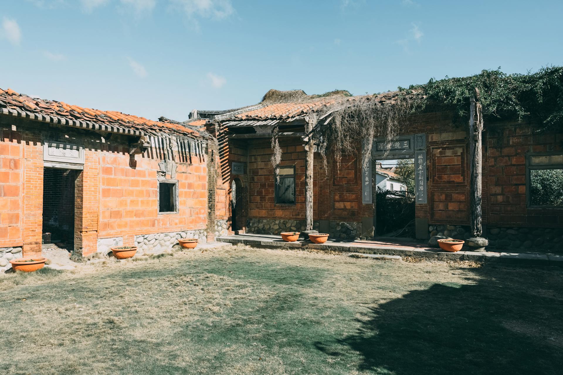 Abandoned brick buildings with damaged roofs under a clear blue sky.