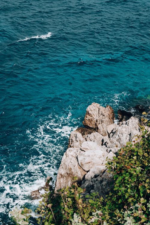 Free A picturesque seashore with rocky formations against a vibrant blue ocean. Stock Photo