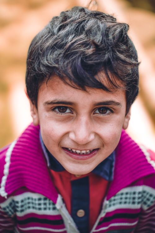 Free Close-up portrait of a smiling boy with brown hair in a colorful sweater, outdoors. Stock Photo