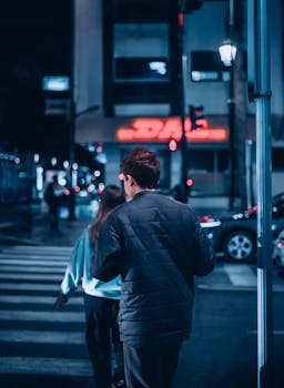 Back view of two people crossing a city street at night under vibrant neon lights.