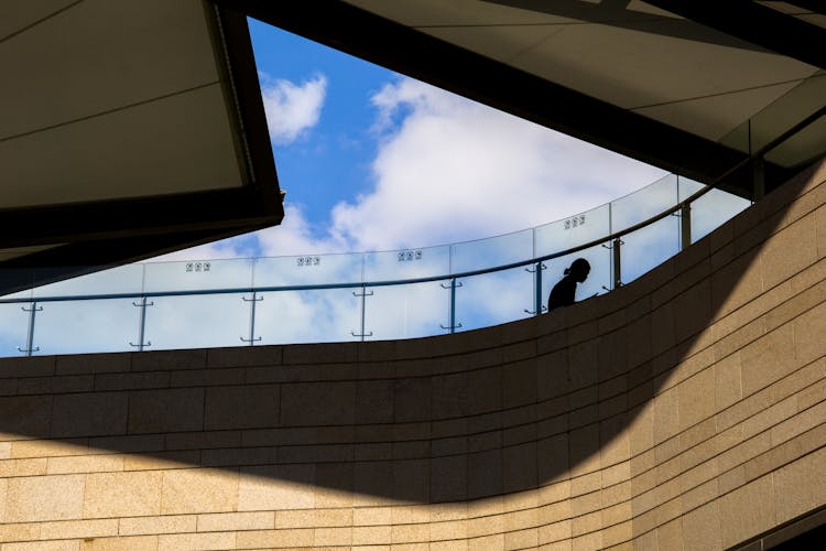 Silhouette Of A Person Sitting Behind A Glass Railing