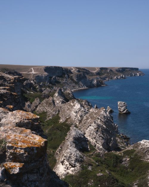 Free A breathtaking view of rocky cliffs and blue sea on a sunny day, perfect for nature lovers. Stock Photo