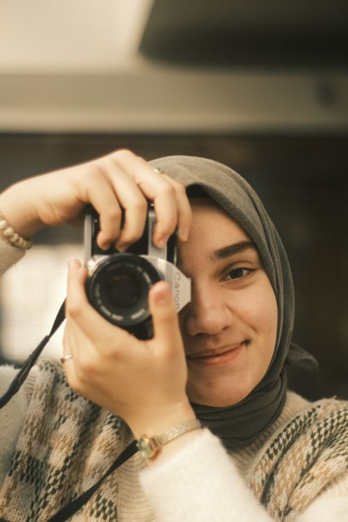 Free Young smiling woman wearing hijab and holding a camera indoors. Stock Photo