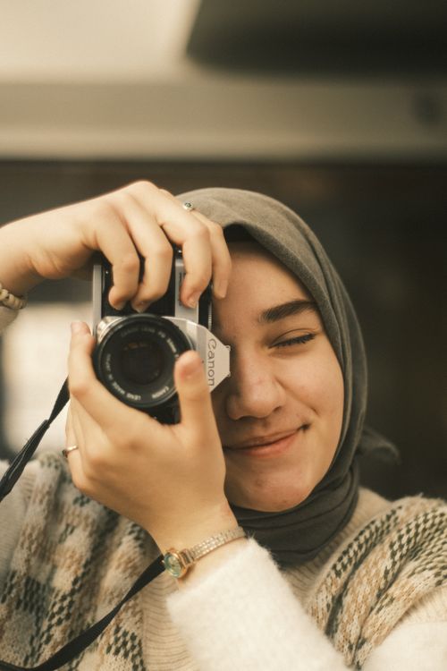 Free Portrait of a young woman in a hijab smiling while taking a photo with a vintage camera. Stock Photo