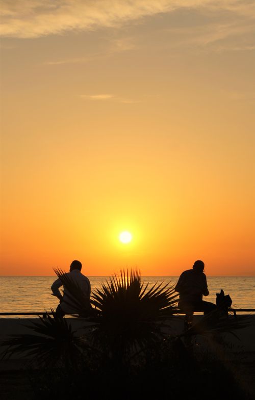 Free Two people silhouetted against a vibrant sunset by the ocean, embodying peace and relaxation. Stock Photo