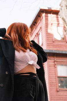 Stylish redhead woman in casual attire posing outdoors against a classic urban building facade.