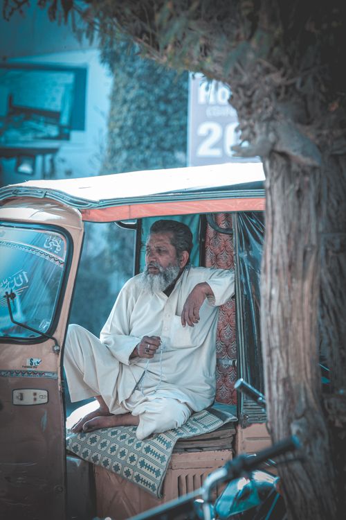 Free A senior man in white attire relaxes in an auto rickshaw on a sunny day in Bahawalpur, Punjab, Pakistan. Stock Photo