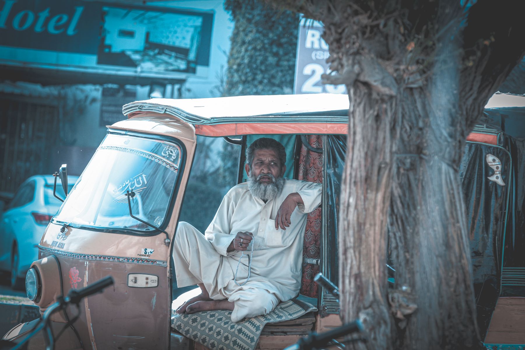 An elderly man with gray hair sits relaxed in an auto rickshaw on a sunny day in Bahawalpur, Pakistan.