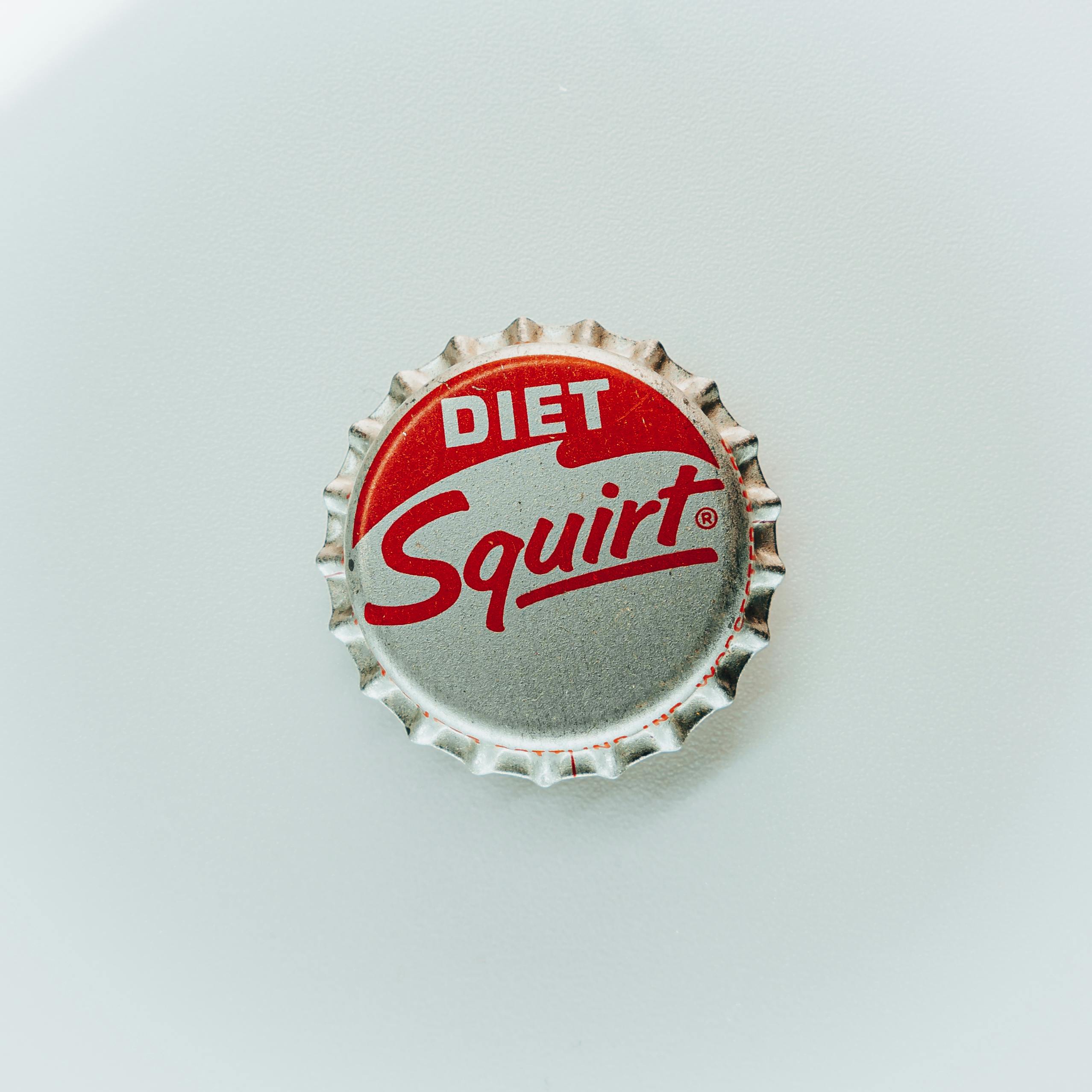 Minimalist closeup of a Diet Squirt bottle cap against a light backdrop, emphasizing design and vintage feel.