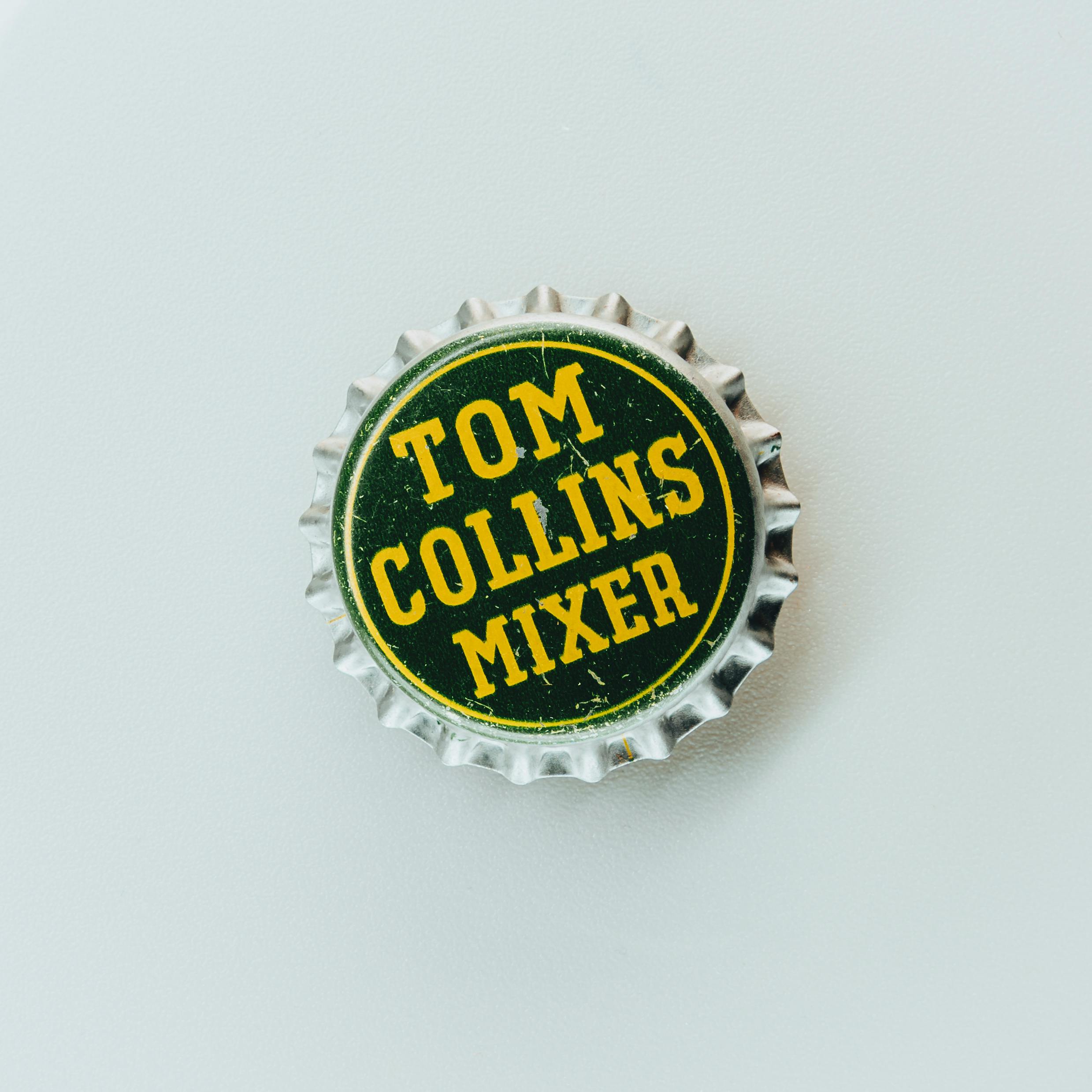 Closeup of a vintage Tom Collins Mixer bottle cap on white background, showcasing classic design.