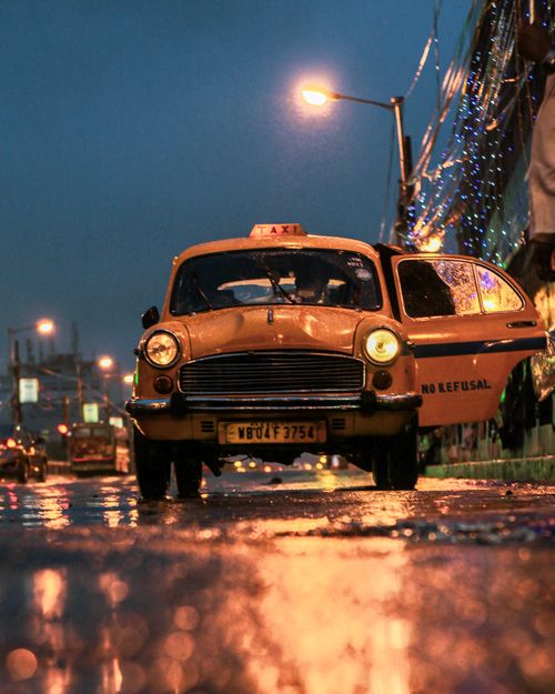 Free A classic yellow taxi on the wet streets of Kolkata at night, reflecting urban life. Stock Photo
