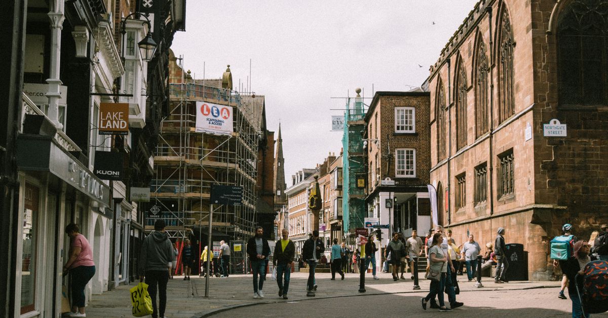 A lively street scene in Chester, England, showing people walking amidst historic buildings.