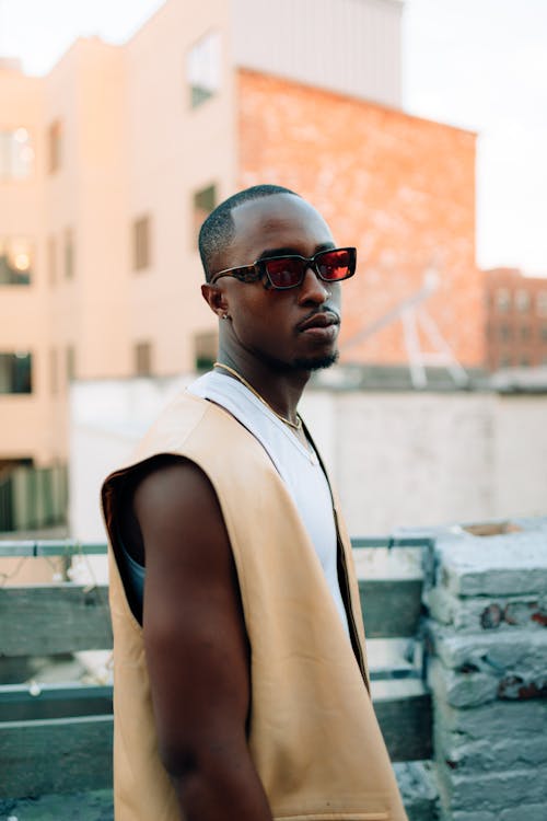 Fashionable Young Man in a Vest and Sunglasses Walking on a Sidewalk in City 