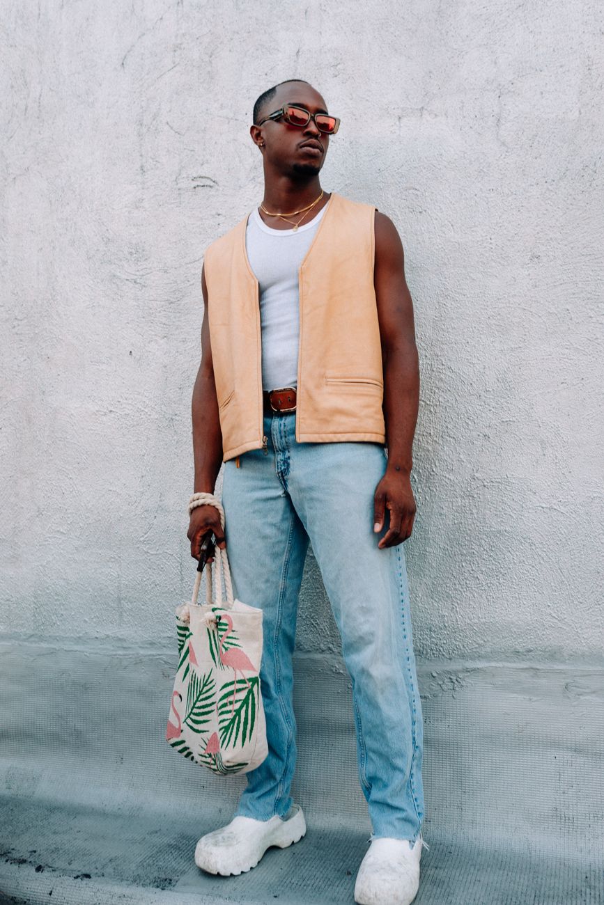 Stylish individual posing with a tropical print bag against a textured wall.