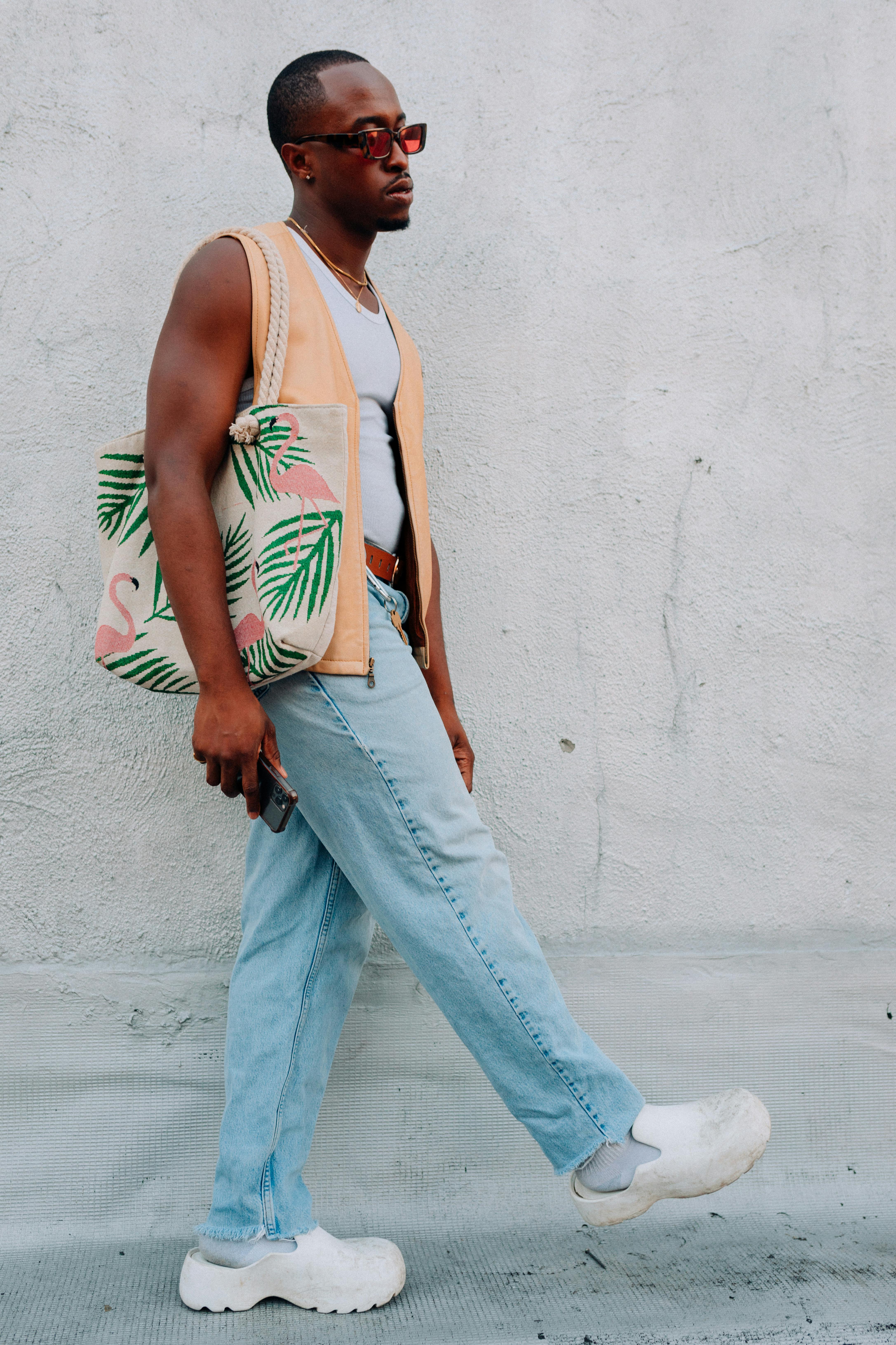 free photo of black man with summer shopping bag posing near wall