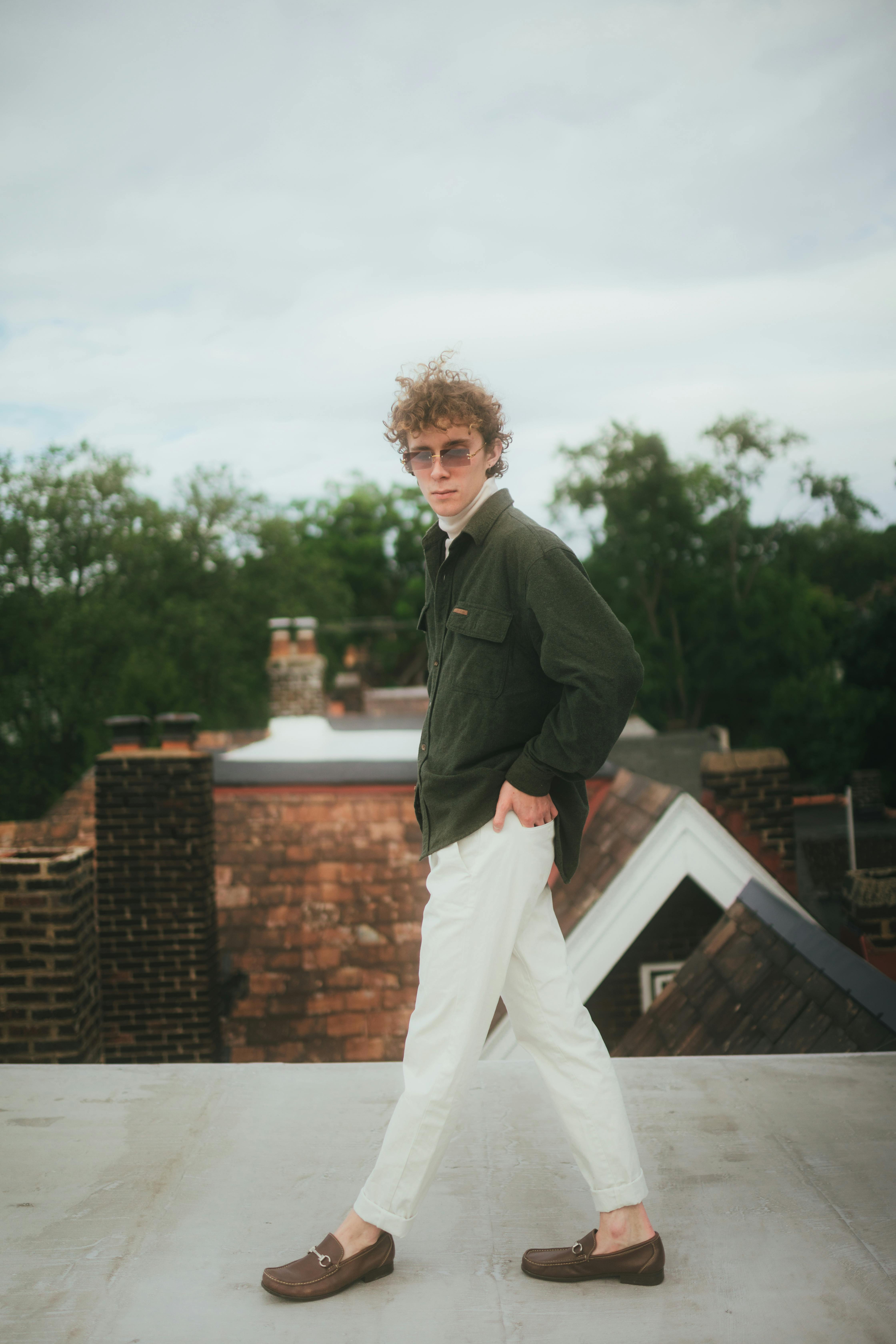 Young man in trendy outfit posing confidently on a rooftop showcasing modern fashion.