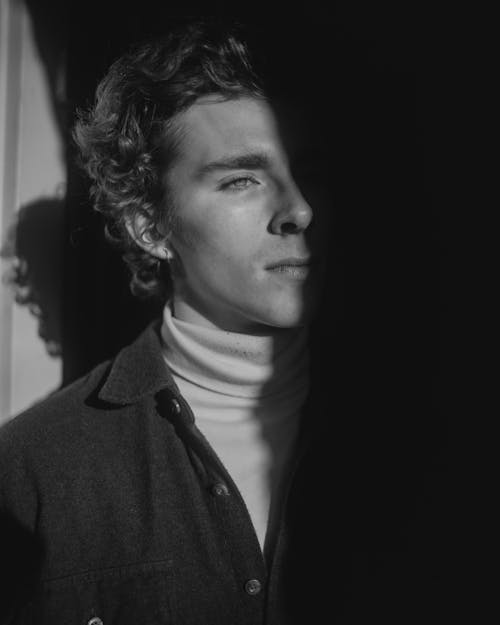 Black and White Photo of a Young Man in a Turtleneck Standing with Half of His Face in Sunlight 