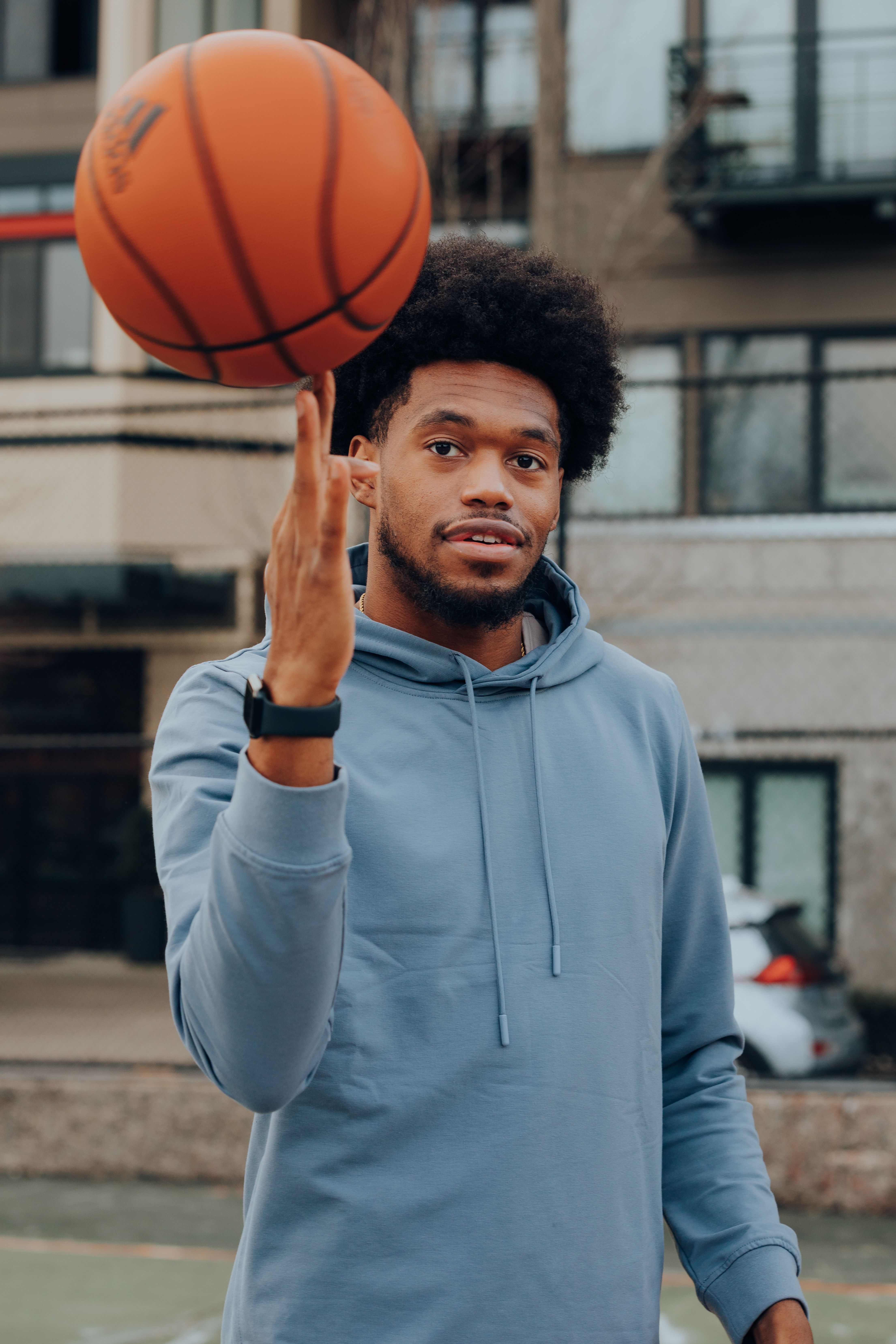 A young man with afro hair skillfully spins a basketball on his finger outdoors.